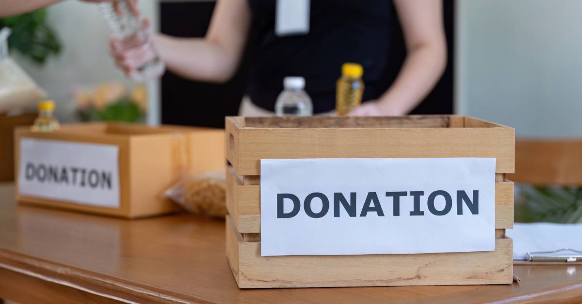 Two wooden boxes with signs saying “Donation” on them are sitting on a brown wooden table next to several bottles.