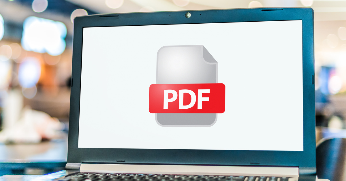 A close-up of a laptop computer displaying the icon of a PDF file. The laptop is on a coffee table in a crowded space.